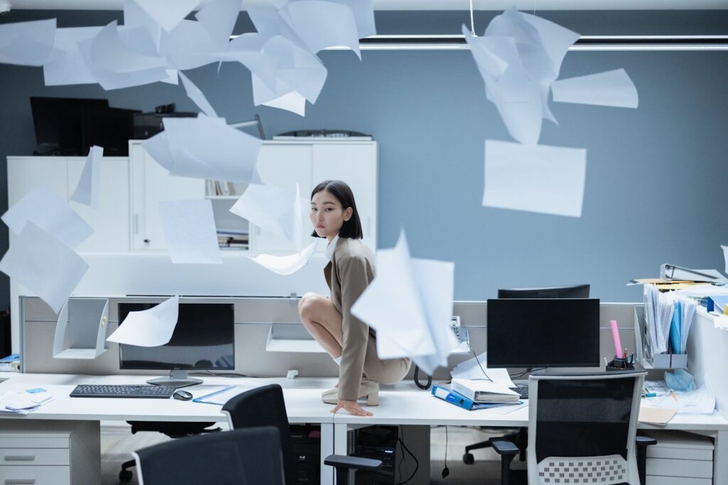 Woman Kneeling on Desk With Flying Papers