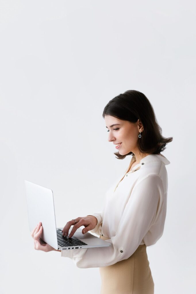 A smiling woman standing and typing on a laptop