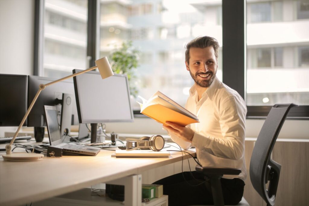 A man seated on his office desk happily reviewing a book or a material