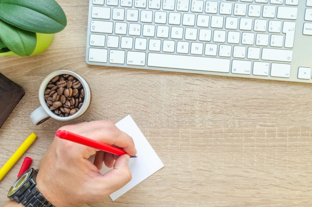 Man writing on a Sticky Note with a Keyboard and Coffee Beans